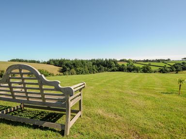 A wooden bench on a lawn overlooking fields and trees at Orchard Retreat in East Worlington near Witheridge