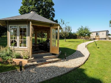 A garden path leading to a wooden gazebo and a mobile home in a grassy area at Orchard Retreat in East Worlington near Witheridge