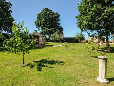 A garden with small trees a path a wooden gazebo and a sundial on a pillar at Orchard Retreat in East Worlington near Witheridge
