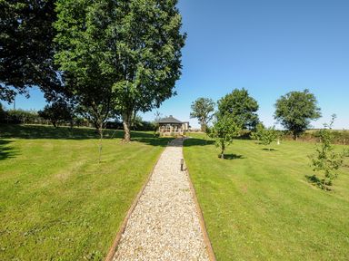 A gravel path through a lawn with trees leading to a small structure at Orchard Retreat in East Worlington near Witheridge