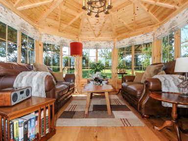 A wooden sunroom with two brown leather sofas a wooden coffee table and windows with patterned blinds at Orchard Retreat in East Worlington near Witheridge