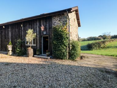 Exterior of a stone and wood building with plants outside and a gravel driveway at Orchard Retreat in East Worlington near Witheridge