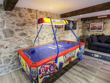 A game room with an air hockey table dartboard stone walls and a sofa at Orchard Retreat East Worlington near Witheridge