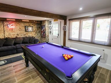 A room with a purple pool table black sofa and stone wall at Orchard Retreat in East Worlington near Witheridge
