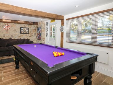 A game room with a purple pool table brown couch stone wall and large window blinds at Orchard Retreat in East Worlington near Witheridge