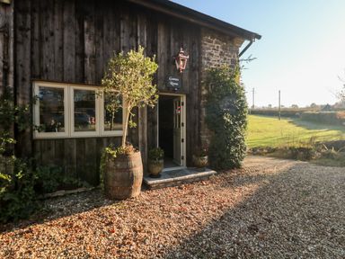The outside of a building with wooden and stone walls a door with a sign saying Games Room and a tree in a barrel at Orchard Retreat in East Worlington near Witheridge