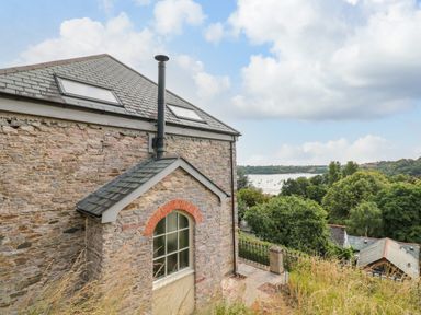 A stone building with two skylights and chimney near a river and trees at The Old Chapel in Dittisham