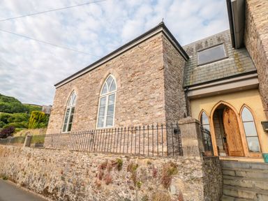 Exterior view of a stone building with arched windows and wooden door with steps at The Old Chapel in Dittisham