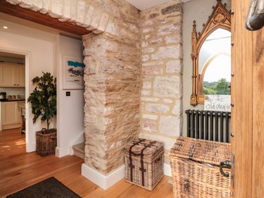 An entryway with stone walls, two wicker baskets, a wooden door, and a mirror above a radiator at The Old Chapel in Dittisham