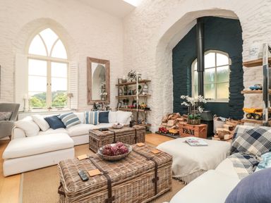 A living room with white stone walls sofas wicker coffee tables and a wood stove at The Old Chapel in Dittisham