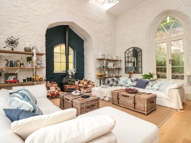 A living room with white sofas wicker chests and shelves with decorations at The Old Chapel in Dittisham