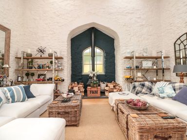 A living room with white sofas wicker coffee tables and shelves with decorations at The Old Chapel in Dittisham