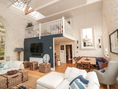 A living room with white sofas wicker baskets and a dining area with wooden table and chairs at The Old Chapel in Dittisham