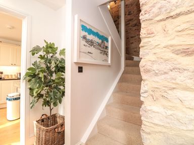 A staircase with carpet next to a stone wall and a potted plant in a basket beside a doorway to a kitchen at The Old Chapel in Dittisham
