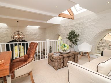 A sitting area with a leather chair, wicker coffee table, white armchair, sofa, and plants at The Old Chapel in Dittisham
