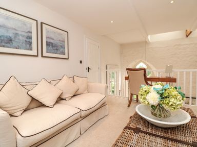 A seating area with a beige sofa and cushions a wicker coffee table with flowers and a study desk with a chair at The Old Chapel in Dittisham
