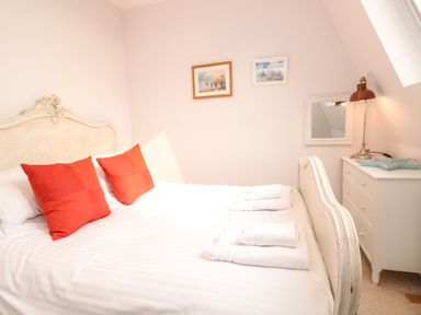 A bedroom with a double bed with red pillows white towels on the bed a white dresser and a lamp at The Old Chapel in Dittisham