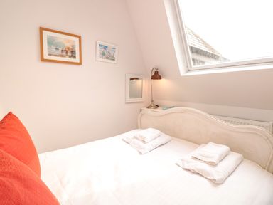 A bedroom with a white bed and red pillows under a slanted window with a lamp and two pictures on the wall at The Old Chapel in Dittisham