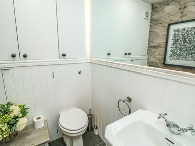 A bathroom with a toilet a sink a small table with flowers and toilet paper and a framed picture on a stone wall at The Old Chapel in Dittisham