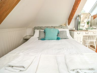 A bedroom with a bed, pillows, folded towels, and a dressing table with a chair at The Old Chapel in Dittisham