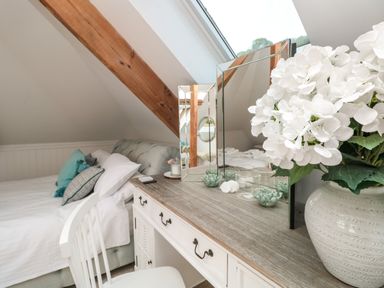 A bedroom with a bed and pillows and a wooden dressing table with a mirror and white flowers at The Old Chapel in Dittisham