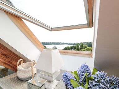 A table with a lamp basket and flowers under a skylight window with a view of trees and water at The Old Chapel in Dittisham