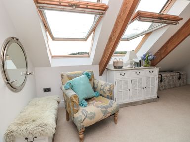 An attic room with a patterned armchair and teal cushion a white cabinet with decorations and two skylight windows at The Old Chapel in Dittisham