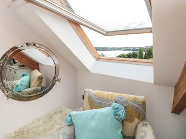 A small seating area with a patterned armchair and turquoise pillow under a skylight window with a view of trees and water at The Old Chapel in Dittisham