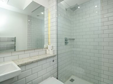A bathroom with a walk in shower a sink a mirror and a granite shelf with toilet paper at The Old Chapel in Dittisham