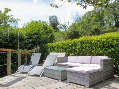 An outdoor seating area with two lounge chairs a wicker sofa and a glass top table surrounded by greenery at The Old Chapel in Dittisham