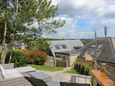A patio with outdoor seating and a glass table overlooking rooftops and greenery at The Old Chapel in Dittisham