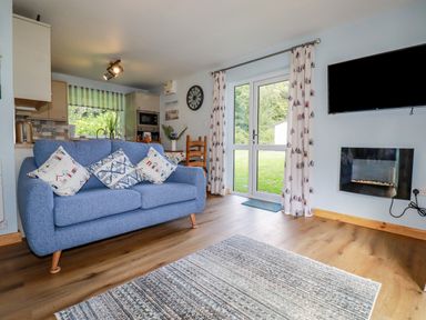 A living room with a blue sofa next to glass doors and a wall-mounted television at Woodside in Rosecraddoc near St Cleer
