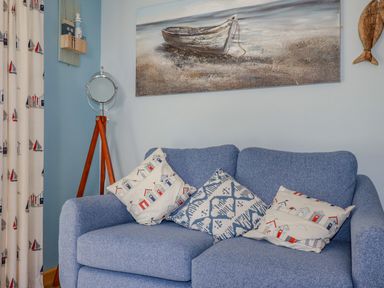 A blue sofa with three decorative pillows a standing mirror a painting of a boat on the wall and curtains with sailboat patterns at Woodside in Rosecraddoc near St Cleer