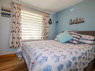 A bedroom with a bed covered in beach hut patterned bedding and nautical decorations on the wall at Woodside Rosecraddoc near St Cleer