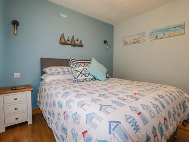 A bedroom with a bed and bedside table with remote controls and wall decorations at Woodside in Rosecraddoc near St Cleer