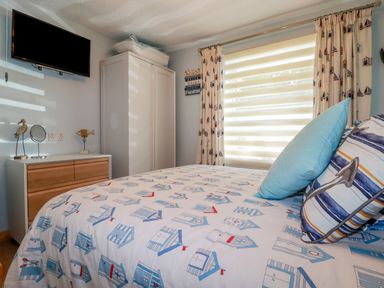 A bedroom with a bed a dresser a wardrobe a wall mounted television and nautical themed curtains and bedding at Woodside Rosecraddoc near St Cleer