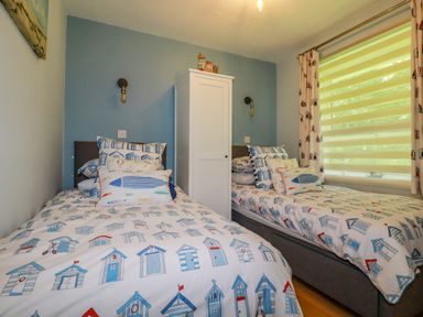 A bedroom with two single beds a white wardrobe and patterned bedding at Woodside in Rosecraddoc near St Cleer