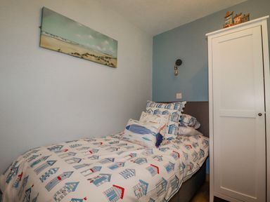 A bedroom with a single bed with printed bedding a white wardrobe wall art and a wall light at Woodside in Rosecraddoc near St Cleer