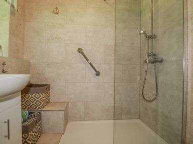 A bathroom with a walk-in shower a mounted showerhead a sink and storage baskets at Woodside in Rosecraddoc near St Cleer
