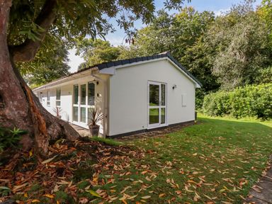 The exterior of a white building with windows and doors surrounded by grass trees and fallen leaves at Woodside in Rosecraddoc near St Cleer