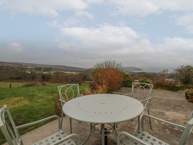 A patio with a round metal table and four chairs overlooking a grassy field and hills at Ceunant near Newport