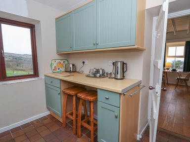 A kitchen area with wooden stools under a counter and a window showing hills at Ceunant near Newport