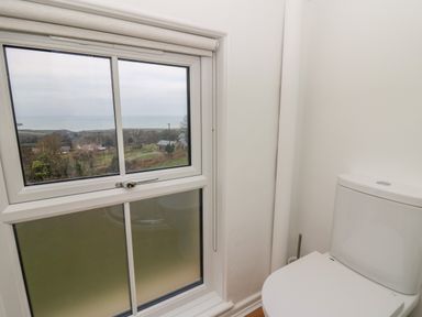 A bathroom with a toilet next to a window showing a countryside and sea view at Ceunant near Newport