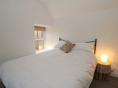 A bedroom with a double bed a patterned cushion a small window and a lit lamp on a round table at Ceunant near Newport