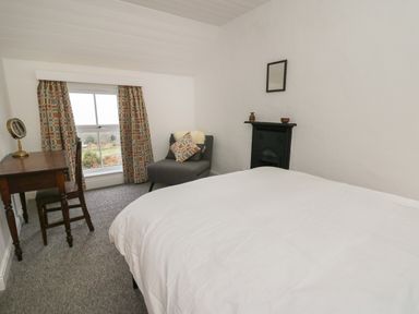 A bedroom with a bed a desk and chair an armchair a window with curtains and a small fireplace at Ceunant near Newport
