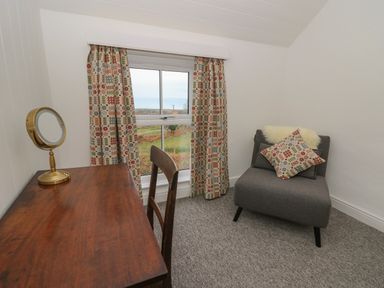A small room with a wooden desk and chair a gray armchair with cushions and a window with patterned curtains at Ceunant near Newport