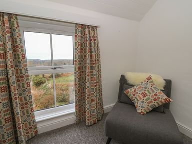 A window with patterned curtains and a grey chair with cushions in a room at Ceunant near Newport