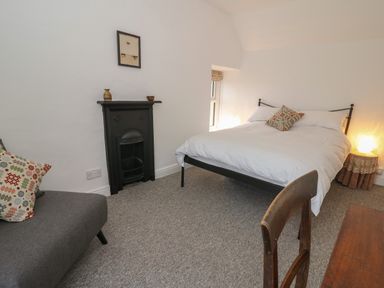 A bedroom with a bed a small fireplace a gray sofa and a wooden chair at Ceunant near Newport