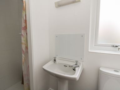A bathroom with a white sink and taps a shower with a curtain a white toilet and a frosted window at Ceunant near Newport