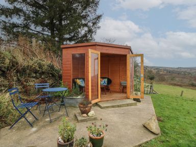 A wooden garden shed with open glass doors and two chairs inside a patio with a blue metal table and chairs near grassy fields at Ceunant near Newport
